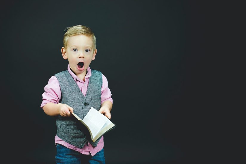 kleines weißer Kind mit erstauntem Gesichtsausdruck, das ein aufgeschlagenes Buch hält.