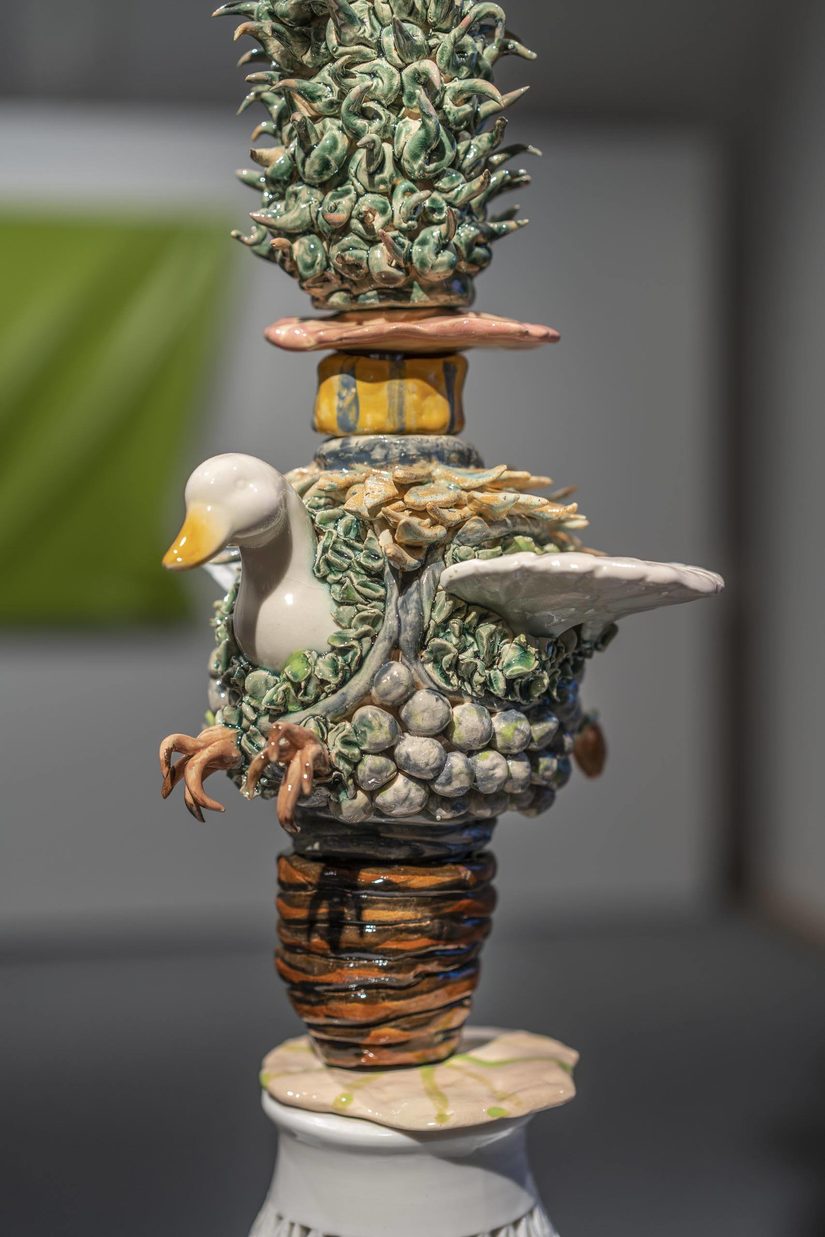 Bildausschnitt einer Keramikskulptur aus verschiedenen Elementen. Im Hintergrund links ist unscharf eine hellgrüne, in Falten geworfene Leinwand zu sehen.