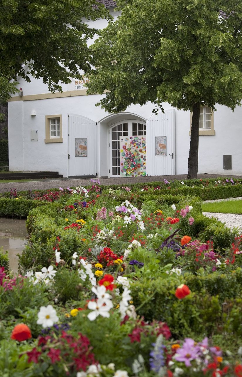 Eingang Reithalle Schloß Neuhaus mit Blumenbeeten im Vordergrund.