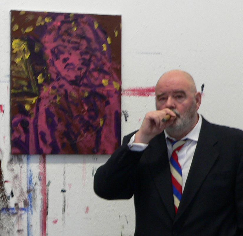 Friedemann Hahn in schwarzen Anzug mit Zigarre im Mund schaut in die Kamera und steht vor einem lilanen Frauenporträt.