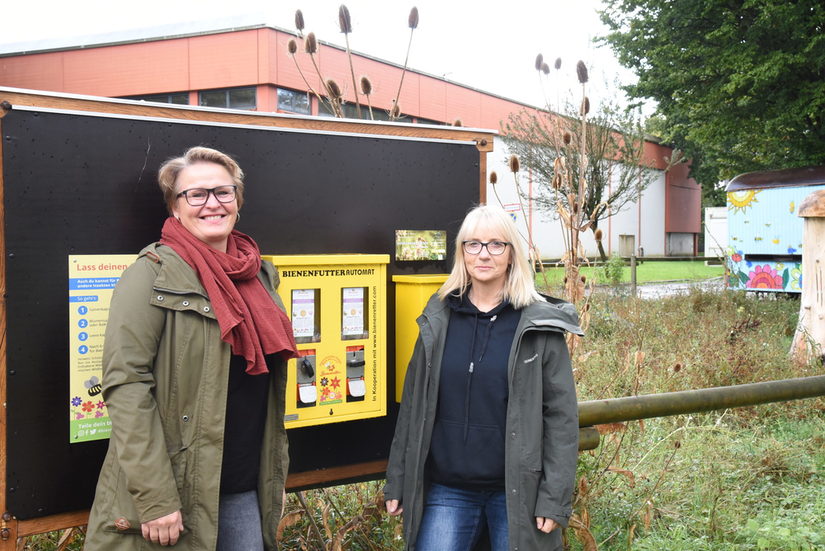 Zwei Frauen stehen neben einem alten Kaugummiautomaten, welcher nun als Spender für Pflanzensamen dient