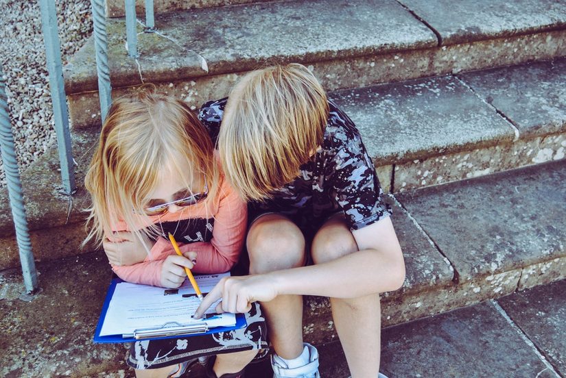 Zwei weiße Kinder beim Lösen eines Rallyebogens auf einer Treppe.