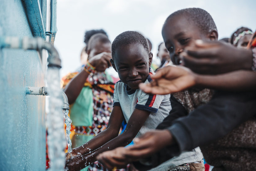 Mehrere Kinder lassen sich Wasser aus einem Hahn über die Hände laufen.