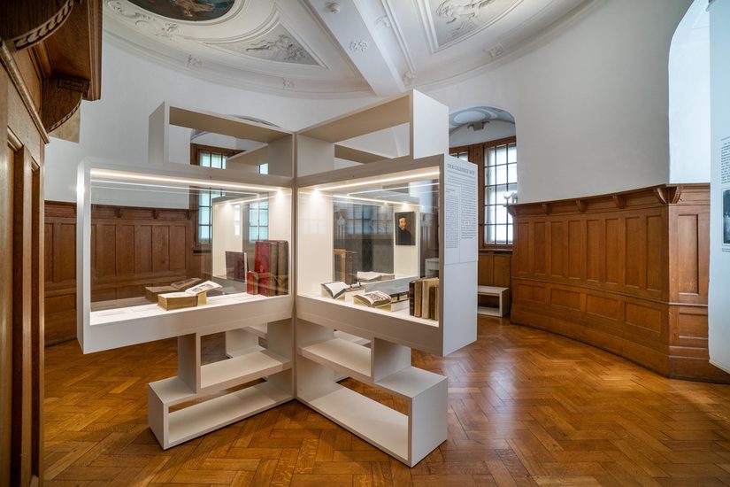 Foto der alten Bibliothek mit hölzerner Wandvertäfelung und einer Ausstellungseinheit mit Büchern in der Mitte.