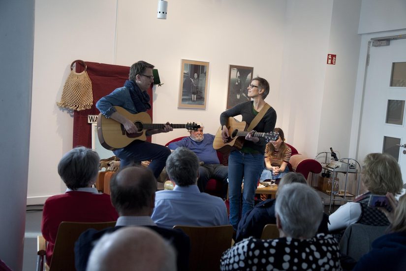 Markus runte und einer Frau spielen Gitarre. Im Hintergrund sitzen Karl und Antje Telgenbüscher.